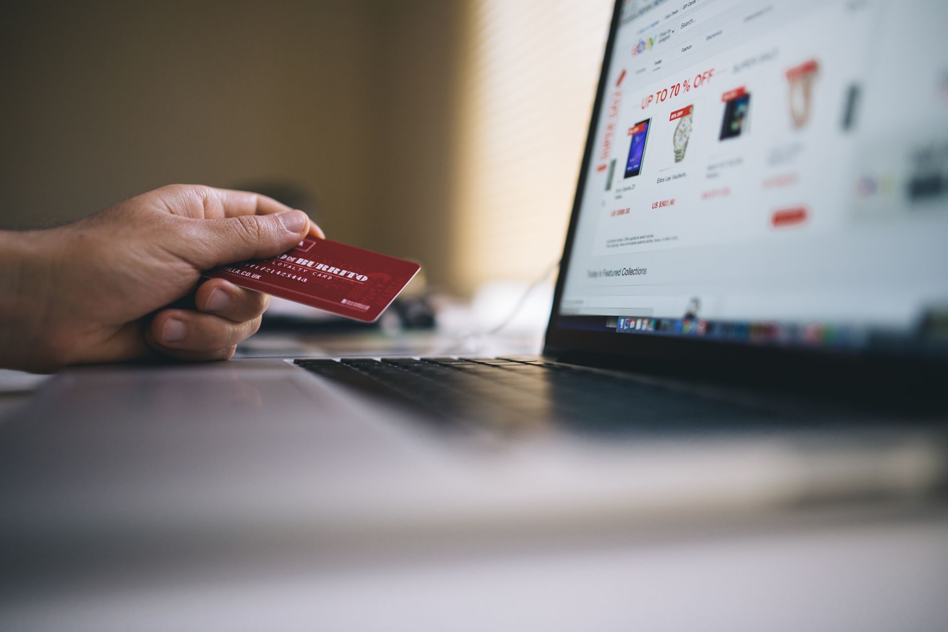 Osoba trzyma kartę płatniczą podczas zakupów online na laptopie